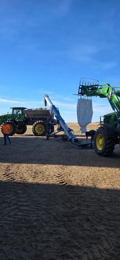 Loader holding a white super sack above field distribution equipment