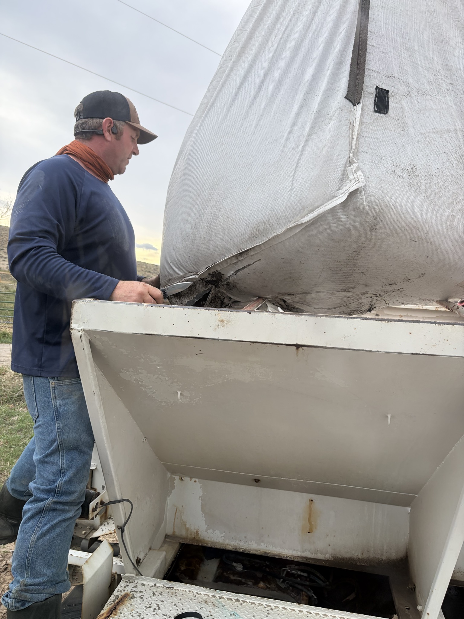Worker positioning a white super sack over field spreading equipment